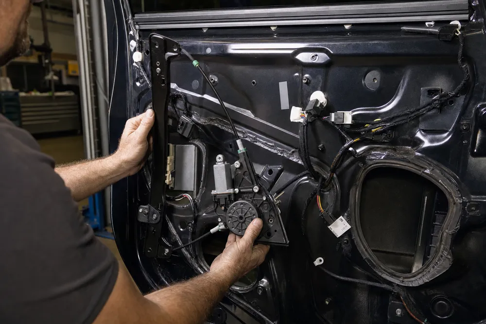Technician installing a new power window regulator inside a car door